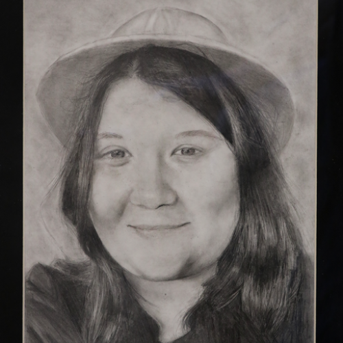 Graphite pencil picture of the artist smiling wearing a hat