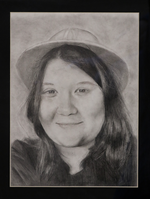 Graphite pencil picture of the artist smiling wearing a hat